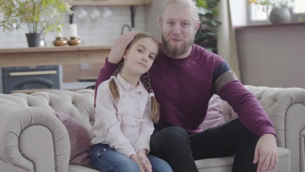 Portret van een blanke vader die dochters liefkoost, naar de camera kijkt en glimlacht. Jongeman en tienermeisje met gevlochten vlechtjes die thuis poseren. Ouderschap, geluk, levensstijl. — Stockvideo