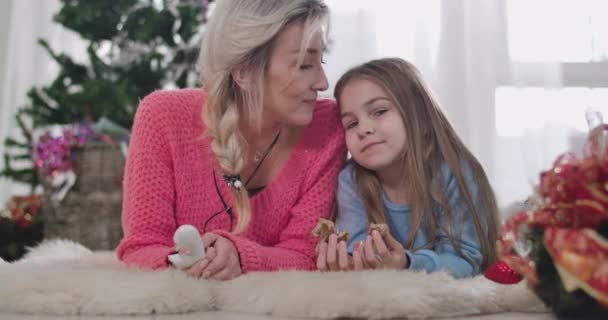 Retrato de cerca de la joven madre caucásica besando a su hija en la frente. Mujer rubia adulta y chica morena pasando la víspera de Navidad juntos en casa. Sede del cine 4k ProRes . — Vídeo de stock