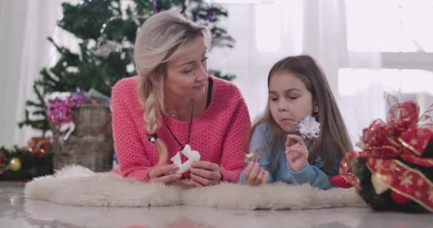 Alegre chica morena caucásica haciendo muecas al comer galletas de Navidad con la madre en casa. Feliz familia pasando la víspera de Año Nuevo en el interior juntos. Sede del cine 4k ProRes . — Vídeo de stock