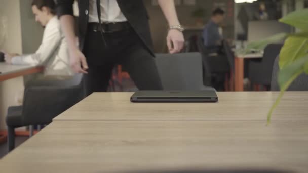 Vista frontal do homem concentrado da ruiva caucasiana sentado na cadeira à mesa e laptop de abertura. Homem confiante em fato preto formal a trabalhar no escritório do espaço aberto. CEO, gestão . — Vídeo de Stock