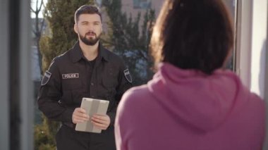 Kapıda tabletle durup esmer kadınla konuşan yakışıklı beyaz polis memurunun portresi. Dedektifler suçu araştırıyor. Görgü tanığı, ifade, koruma, sorgulama.