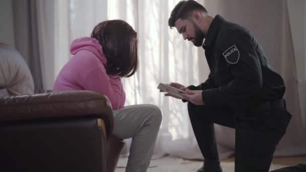 Side view of brunette Caucasian young woman telling police officer about details of robbery. Detective recording information with the use of tablet. Law enforcement, security, break-in, investigation. — Stock Video