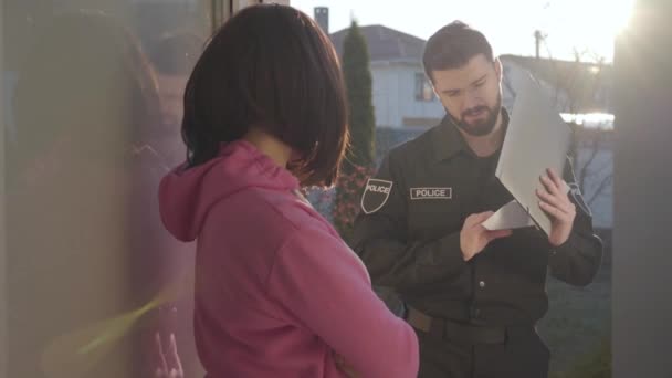 Jóképű kaukázusi rendőr áll napsugarakban dokumentumokkal és barna nővel beszél. Fiatal nyomozó nyomoz a bűnügyben. Tanúskodás, kihallgatás. — Stock videók