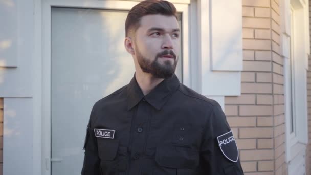 Der junge kaukasische Detektiv schaut sich um und klopft an die Haustür. Mann mit braunen Augen und Bart auf Polizeistreife. Vollzugsbeamte, Polizisten. — Stockvideo
