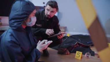 Kafkasyalı genç polis memurunun portresi ve olay yerinde konuşan adli araştırmacı. Dedektifler kanıtları tartışıyor. Profesyoneller, kriminoloji, suikast.