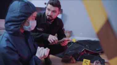 Tablet tutan ve adli araştırmacılarla konuşan sakallı beyaz bir polis memurunun portresi. Profesyoneller öldürülen cesedin yanında oturan suçları tartışıyor. Soruşturma, kolluk kuvvetleri.