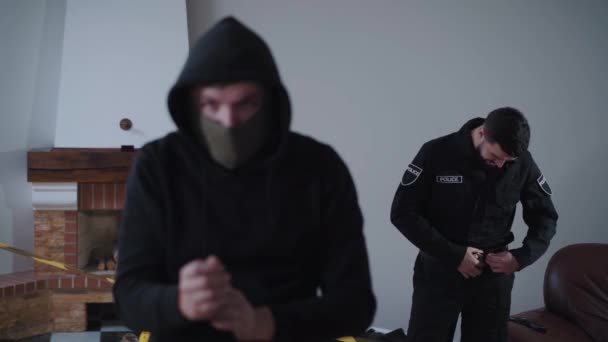 Verschwommener kaukasischer Kriminalist, der die Hände hinter den Kopf legt, als lächelnder Polizist, der im Hintergrund seine Uniform fixiert. Profi ertappt Räuber am Tatort Detektiv im Fokus. — Stockvideo