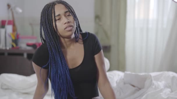 Jovem afro-americana sentada na cama, consertando dreadlocks, e saindo. Retrato de mulher bonita acordando de manhã em casa. Estilo de vida, lazer . — Vídeo de Stock