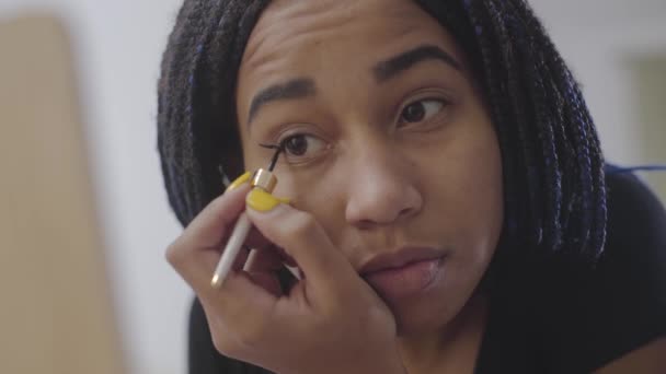 Close-up rosto de menina afro-americana desenhando setas dos olhos. Adolescente confiante com dreadlocks olhando para o espelho e fazendo seu rosto. Beleza, cuidado do rosto, estilo de vida . — Vídeo de Stock