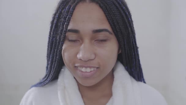 Retrato de mulher afro-americana positiva com dreadlocks olhando para a câmera e sorrindo. Uma adolescente bonita de roupão branco a posar. Beleza, estilo de vida . — Vídeo de Stock