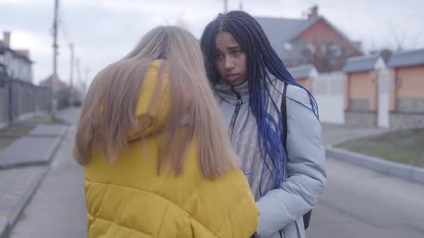 Junge afrikanisch-amerikanische Frau zeigt Dreadlocks und spricht mit blonden Mädchen. beleidigter Teenager geht, Kaukasierin bleibt allein auf der Straße. — Stockvideo