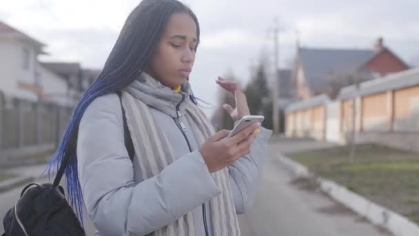 Portrait de jeune jolie afro-américaine debout dans la rue avec smartphone et regardant autour. Adolescent perdu en utilisant des cartes en ligne. Technologies modernes, sans fil . — Video