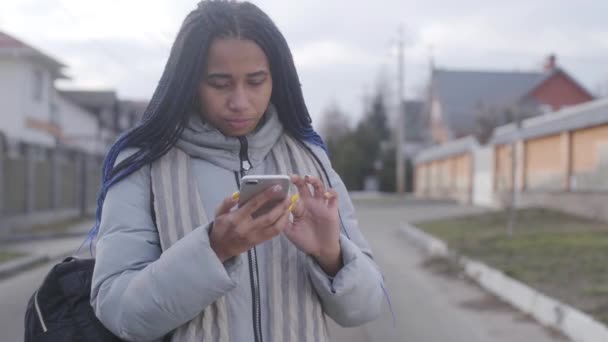Mooi Afrikaans Amerikaans meisje met dreadlocks die op straat staan en smartphone gebruiken. Slimme tiener die sociale media buiten gebruikt. Draadloze technologieën, online. — Stockvideo
