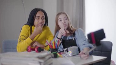 Birlikte video bloğu yapan iki arkadaşın portresi. Kafkas ve Afrikalı Amerikalı genç kızlar akıllı telefon ekranına bakıyor ve konuşuyorlar. En iyi arkadaşlar içeride dinleniyor..