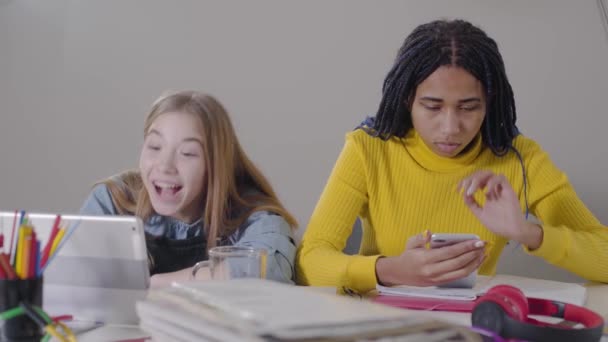 Piękna biała dziewczyna, która ma rozmowę wideo na tablecie, patrzy na zdenerwowanego Afroamerykanina i uspokaja ją. Smutna kobieta z dredami patrząc na ekran smartfona trzymając głowę rękami. — Wideo stockowe