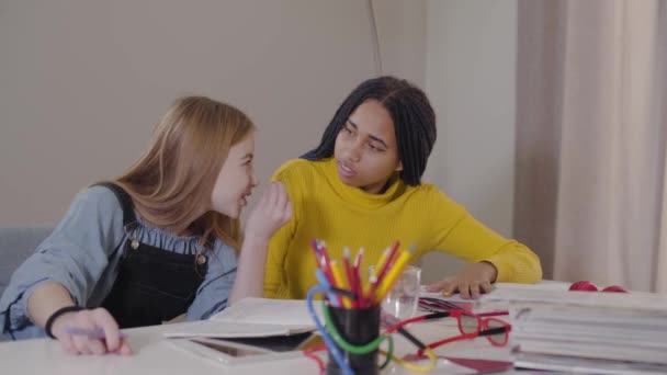 Retrato de una mujer afroamericana escuchando a una amiga caucásica. Adolescente haciendo deberes juntos en interiores y comunicándose. Estudiar, educar . — Vídeo de stock