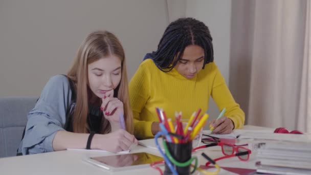 Vista lateral de dois amigos fazendo lição de casa em casa. Menina afro-americana fazendo gesto de vitória e dando mais cinco ao amigo caucasiano. Estudantes a estudar juntos. Conceito de educação . — Vídeo de Stock