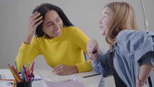 Retrato de una hermosa mujer afroamericana escuchando a su amiga caucásica hablando emocionalmente. Estudiantes felices descansando durante la tarea en casa. educación, diversión, estilo de vida . — Vídeos de Stock