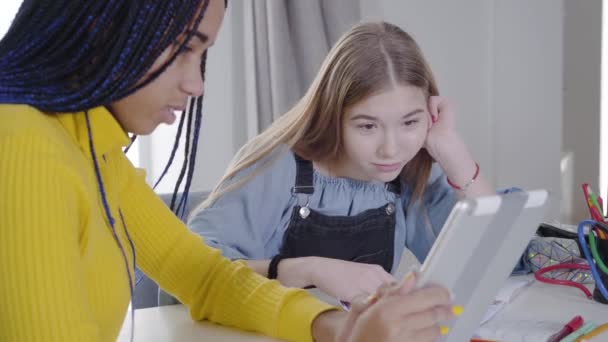 Ritratto di ragazza caucasica guardando lo schermo della tavoletta e gesticolando. Consultazione di adolescenti afroamericani con la migliore amica. Adolescenza, piacere, stile di vita . — Video Stock