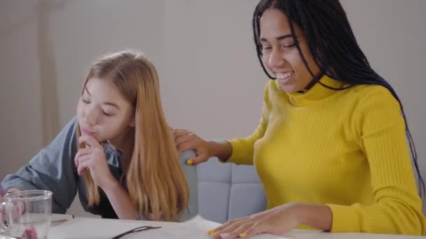 Portret van een blank meisje dat huiswerk maakt als haar Afro-Amerikaanse vriendin die een overwinningsgebaar maakt. Twee studenten die high five geven en glimlachen. Onderwijs, intelligentie, levensstijl. — Stockvideo