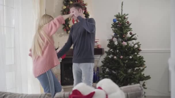 Homem e mulher caucasianos jovens dançando na frente da árvore de Natal em casa. Casal positivo passando a véspera de Ano Novo juntos. Feriados, celebração, felicidade . — Vídeo de Stock