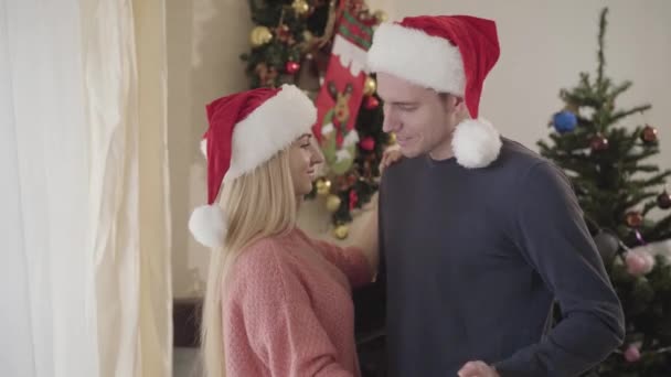 Primer plano del hombre y la mujer caucásicos bailando frente al árbol de Año Nuevo en casa. Feliz joven pareja descansando juntos en Nochebuena. Celebración, vinculación, temporada de fiestas . — Vídeos de Stock