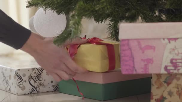 Detailní záběr, mužské bělošské ruce dávají pod novoroční stromek dva zabalené vánoční dárky. Člověk se připravuje na svátky. Oslava, dary, zázrak. — Stock video