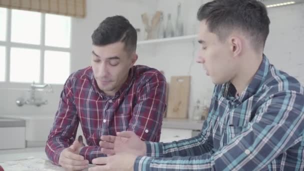 Hermanos gemelos caucásicos sentados a la mesa y discutiendo sobre viajes futuros. Retrato de hermanos adultos planeando vacaciones juntos, mapa acostado sobre la mesa. Viajar, preparación, estilo de vida . — Vídeo de stock