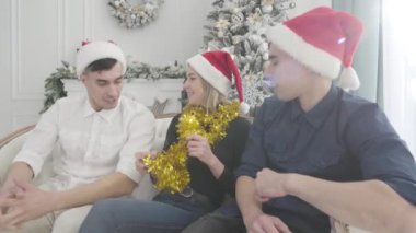 İkiz kardeşler güzel bir kızın her iki tarafında oturuyor ve konuşuyorlar. Arkadaşlarının konuşmalarını dinleyen gülümseyen genç bir kadın. Tatiller, Noel, mutluluk.