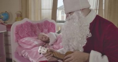 Bulanık beyaz kız sabah uyandığında Noel Baba 'yı pembe yatağında ukulele çalarken görüyor. Baba sürpriz kızı Noel arifesinde. Sinema 4k Prores Merkezi.