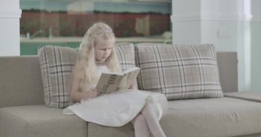 Zarif beyaz elbiseli, koç koltuğunda oturan ve arka planda Noel Baba olarak kitap okuyan güzel beyaz kız. Evde Noel mucizesini bekleyen taç giymiş şirin bir çocuk. Sinema 4k Prores Merkezi.