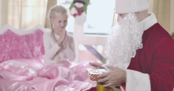 Niña caucásica borrosa frotándose las manos en el fondo mientras Santa Claus le da su regalo de Navidad. Chica abrazando al hombre adulto en traje de Año Nuevo. Sede del cine 4k ProRes . — Vídeos de Stock