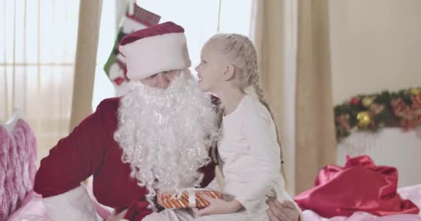 Retrato de Papai Noel segurando menina loira de joelhos e rindo junto com a criança. Criança alegre conversando com o Papai Noel em seu quarto sentado na cama rosa. Natal, férias, infância. Cinema 4k ProRes HQ . — Vídeo de Stock