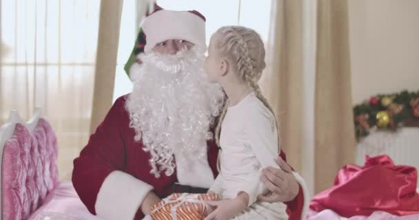 Portret van een volwassen blanke man in Santa Claus kostuum met valse baard die een schattig meisje op de knieën houdt, kind dat hem wensen vertelt. Kerstman geschokt door kinderdromen. Feestdagen, Kerstmis. Bioscoop 4k Prores Hq. — Stockvideo