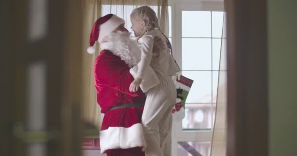 Porträtt av glad vit man i jultomte kostym hålla söt vit barn. Leende flicka i pyjamas ha kul med tomten på julafton. Cinema 4k Prores Hq. — Stockvideo