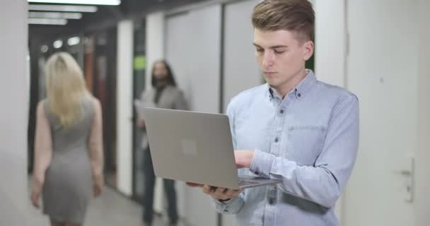 Retrato del joven hombre caucásico escribiendo en el teclado del portátil, mirando a la cámara y sonriendo. Trabajador de oficina seguro de pie en el espacio abierto. Negocios, éxito, trabajo duro. Sede del cine 4k ProRes . — Vídeo de stock