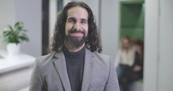 カメラを見て笑顔で正式なビジネススーツで長い巻き毛を持つ幸せな中東の男の肖像画。オープンスペースに立つハンサムな男性のオフィスワーカー。Cinema 4k Prores｜Hq. — ストック動画
