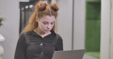 Laptop klavyesinde yazı yazan, kameraya bakıp gülümseyen kendine güvenen kızıl saçlı kadının yakın çekimi. Açık uzay ofisinde poz veren başarılı genç iş kadını. Sinema 4k Prores Merkezi.