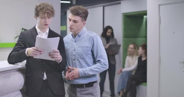 Young Caucasian men standing with laptop in open space office and talking. Team of office workers discussing business project. Cinema 4k ProRes HQ. — Stock Video