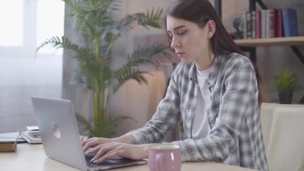 Sérieux jeune fille caucasienne tapant rapidement sur le clavier de l'ordinateur portable. Femme indépendante confiante travaillant en ligne depuis la maison. Freelance, travail à distance . — Video