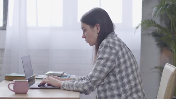 Zijaanzicht van jonge blanke meisje typen snel op laptop toetsenbord. Serieuze vrouwelijke freelancer die online werkt vanuit huis. Freelance, werk op afstand. — Stockvideo