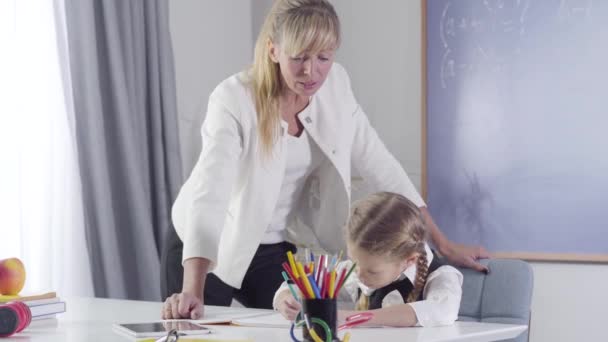 Retrato de tutor de meia-idade caucasiano confiante ao lado de estudante escrevendo em caderno de exercícios. Mulher de meia-idade ensinando criança diligente em casa. Educação, ensino, aprendizagem . — Vídeo de Stock