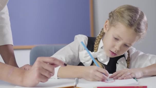 Onherkenbare volwassen vrouwelijke tutor toont iets aan mooie blanke meisje tekening in het oefenboek. Gelukkig kind dat thuis studeert. Diligentie, geluk, onderwijs. — Stockvideo