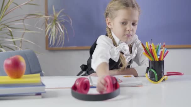 Retrato de una hermosa chica caucásica poniéndose auriculares, haciendo un gesto de victoria y sacudiendo la cabeza. Feliz niño alegre descansando como haciendo la tarea en casa. educación, felicidad, estudio . — Vídeos de Stock