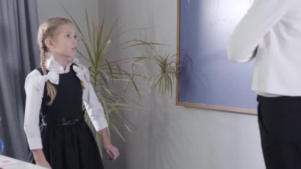 Retrato de menina branca bonita em uniforme escolar elegante e tutor irreconhecível em pé na lousa e estudando. Estudante bonito estudando em casa. Educação, diligência, aprendizagem . — Vídeo de Stock