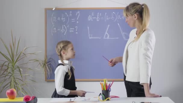 エレガントな学校の制服と黒板に立って、数学を学ぶ中年の家庭教師でかなり白人の女の子の肖像画。家で勉強する聡明な女子高生。教育、勤勉. — ストック動画