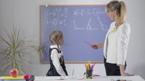 黒板からカメラに背を向けて親指を立てている白人の少女と大人の女性。家庭で数学を学ぶ女子高生と中年家庭教師。教育、勤勉、教育、勉強. — ストック動画