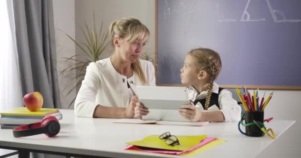 Medelålders kaukasiska kvinna och liten skolflicka sitter vid bordet med tablett och lärande matematik. Utbildning, intelligens, flit, privatundervisning, handledare. Cinema 4k Prores Hq. — Stockvideo