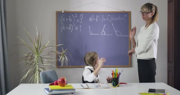 Estudante branca bonito olhando para trás no quadro negro, voltando-se para a câmera e colocando a cabeça nas mãos. Mulher de meia-idade ensinando matemática para criança cansada. Inteligência, educação. Cinema 4k ProRes HQ . — Vídeo de Stock