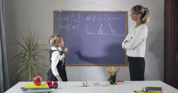 Chica bastante caucásica en elegante uniforme escolar y tutor de mediana edad de pie en la pizarra y el aprendizaje de las matemáticas. Bonita colegiala estudiando en casa. Educación, diligencia. Sede del cine 4k ProRes . — Vídeos de Stock